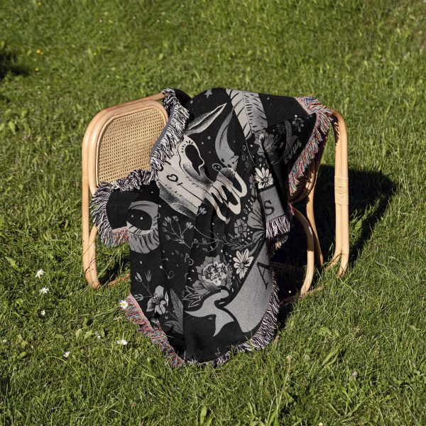 Aries Spirit woven blanket draped over a chair on grass, showcasing buffalo skull design.