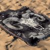 Aries Spirit woven blanket with buffalo skull and floral design lying on sandy surface.