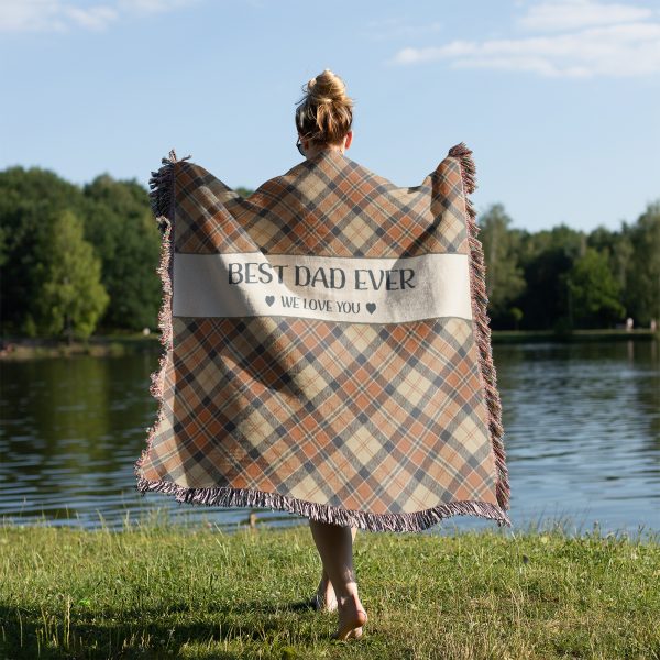 Woman with her back turned, wrapped in the "Best Dad Ever" blanket, showing its size and plaid pattern in orange and beige shades.