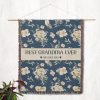 The "Best Grandma Ever" blanket hanging on a wall as a tapestry, showcasing its elegant floral design and wording.