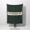 Woman holding up the fully unfolded "Best Grandpa Ever" blanket with a green plaid pattern; her face is not visible.