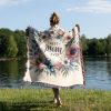 Woman, wrapped in the "Best Mom Ever Bloom Woven Blanket," highlighting its cozy design and emotional message.