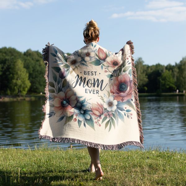 Woman, wrapped in the "Best Mom Ever Bloom Woven Blanket," highlighting its cozy design and emotional message.