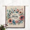 The "Best Mom Ever Bloom Woven Blanket" displayed on a wall as a tapestry, emphasizing its elegant floral design and heartfelt text.