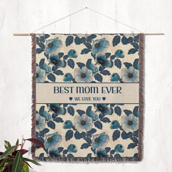 The "Best Mom Ever" blanket hanging on a wall as a tapestry, showcasing its elegant floral design and wording.