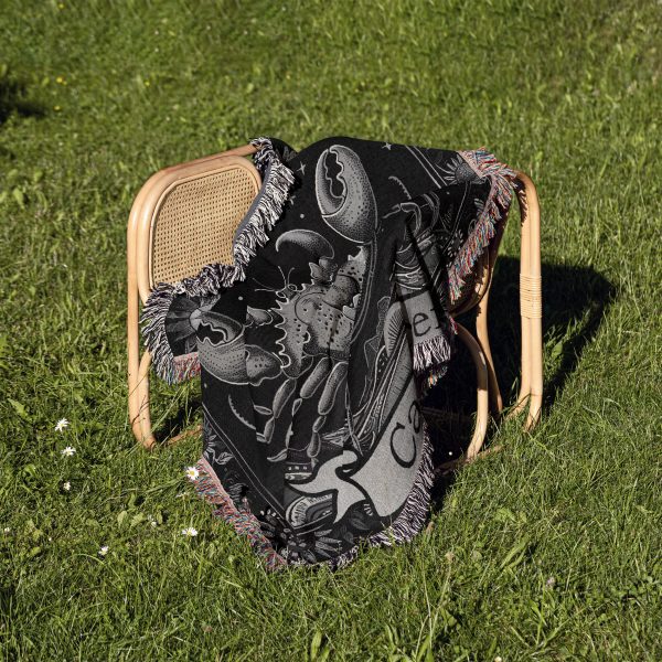 Cancer Spirit woven blanket draped over a chair on grass, showing crab and skull design.