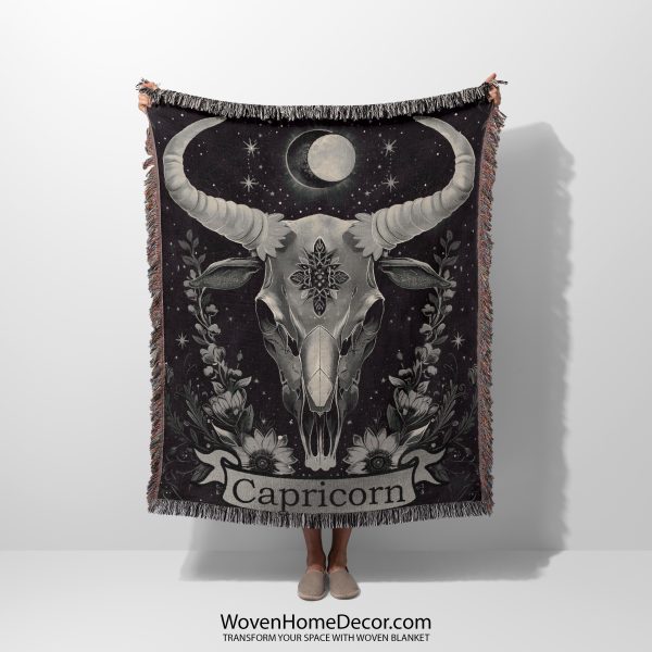 Woman holding the Capricorn Resilience woven blanket with goat skull design; woman not visible.