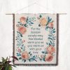 The "Dearest People Woven Blanket" hanging as a wall tapestry, displaying the floral wreath and meaningful text in an artistic setting.