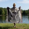 Woman wrapped in Gemini Duality woven blanket, twin skeleton design visible from behind.