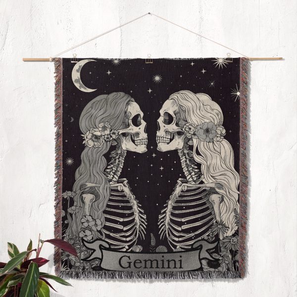 Gemini Duality woven blanket hung on wall as tapestry, showcasing twin skeletons and floral accents.