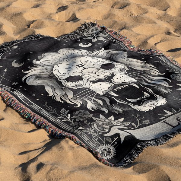 Leo Majesty woven blanket with lion skull lying on sandy surface.