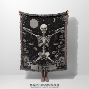 Woman holding the Libra Balance woven blanket with skeleton holding scales; woman not visible.