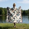 Back view of woman wrapped in Ocean Bloom Woven Blanket with blue flowers, cozy floral pattern on white.