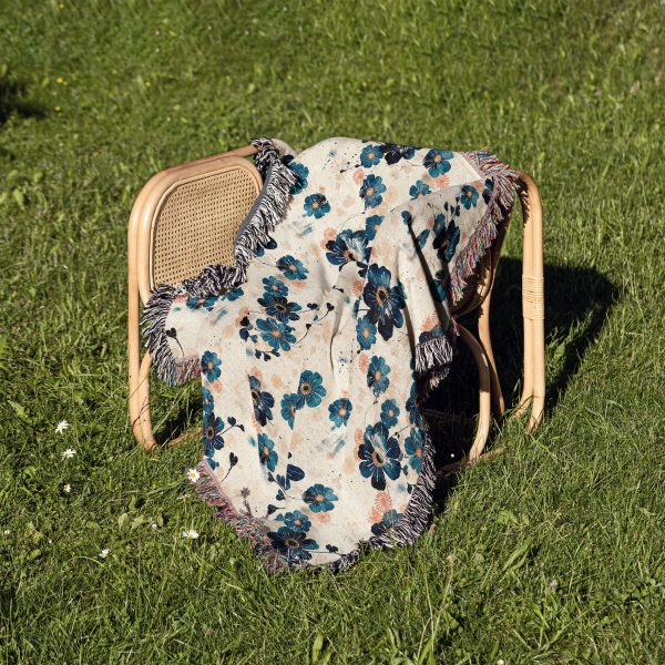 Ocean Bloom Woven Blanket on chair in outdoor setting, blue flowers on white creating a natural, serene look.