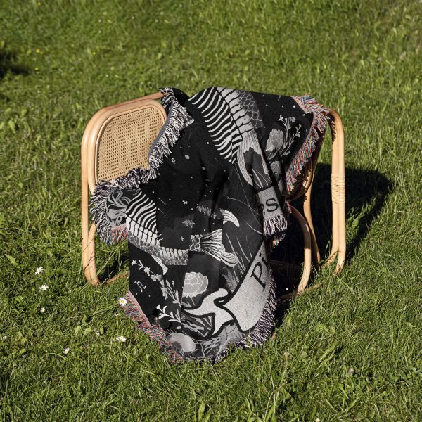 Pisces Dream woven blanket draped over a chair on grass, showing twin fish skeletons.