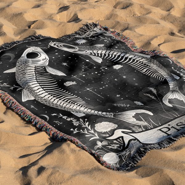 Pisces Dream woven blanket with fish skeletons lying on sandy surface.