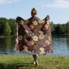 Woman wrapped in floral woven blanket, back view, with large flower patterns in vivid colors.