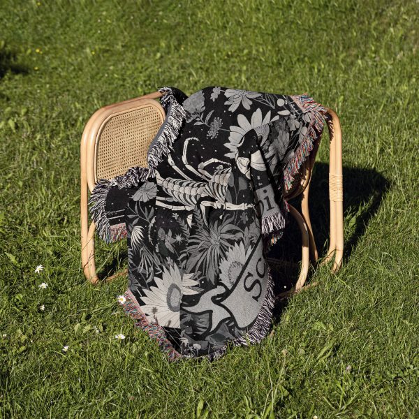 Scorpio Mystery woven blanket draped over a chair on grass, showcasing scorpion design.