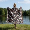 Woman wrapped in floral woven blanket, back view, with bold, bright flowers in vivid, contrasting colors.