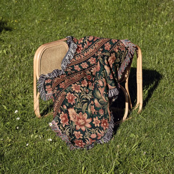 Indian style woven blanket resting on chair outdoors, blending with natural surroundings and colorful patterns.