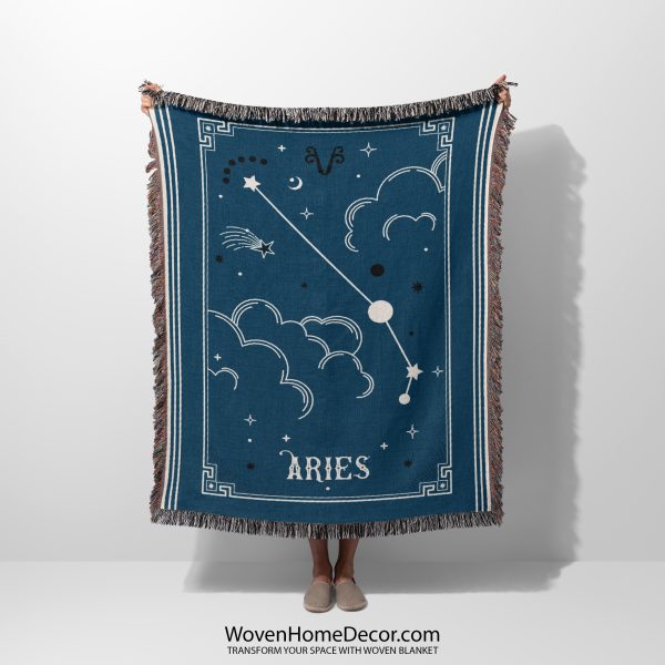 A person holding a woven blanket with the Aries zodiac constellation design, featuring bright red and fiery cosmic elements.