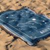 The zodiac woven blanket lies on the sand