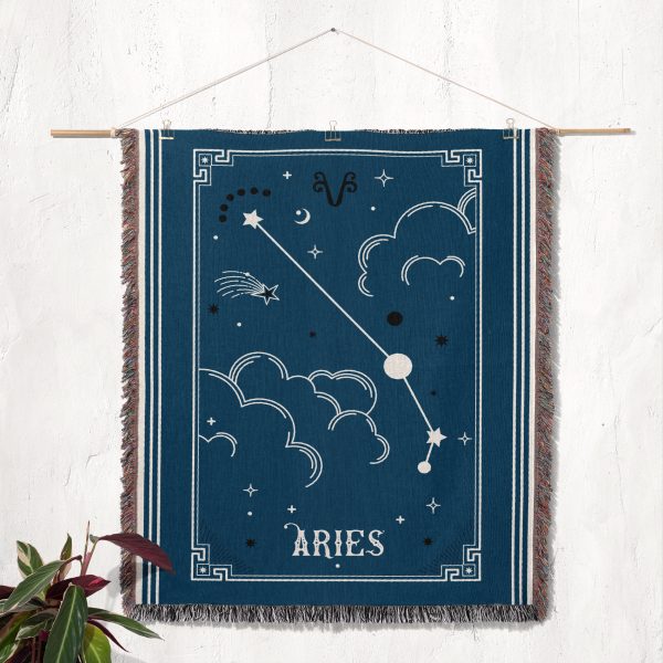 The Aries zodiac woven blanket hanging as a tapestry on the wall, displaying the constellation with bright stars against a striking red background.