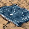 The zodiac woven blanket lies on the sand