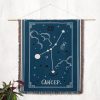 The Cancer zodiac woven blanket hanging as a tapestry on the wall, displaying the crab constellation surrounded by starry accents in soft, calming colors.