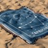 The zodiac woven blanket lies on the sand