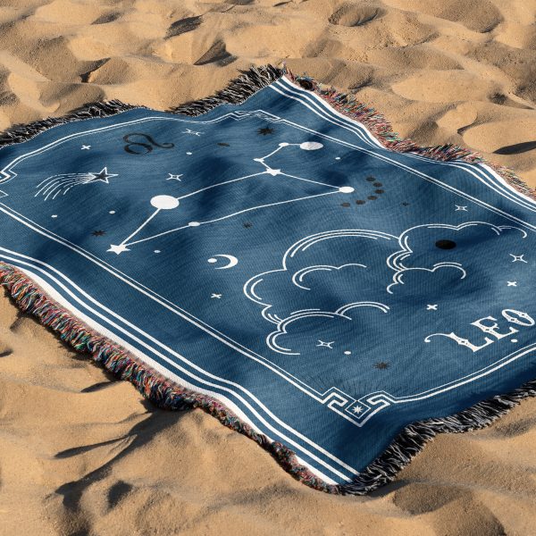 The zodiac woven blanket lies on the sand