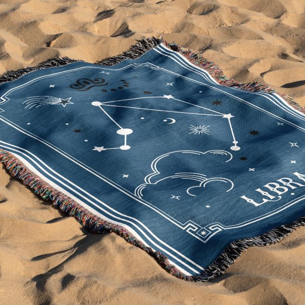 The zodiac woven blanket lies on the sand