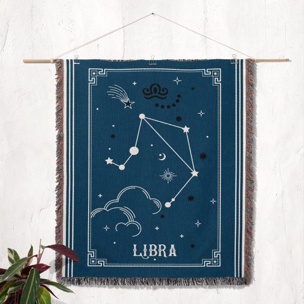 The Libra zodiac woven blanket hanging as a tapestry, showcasing the balance scale and celestial accents in soothing pink and blue tones.