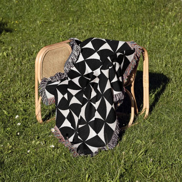 Modern Geometric Woven Blanket folded on a chair outdoors on grass, highlighting its modern style.