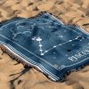 The zodiac woven blanket lies on the sand