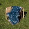 The Pisces zodiac woven blanket resting on a chair in the grass, with its soft blue and turquoise colors blending beautifully with the natural outdoor setting.