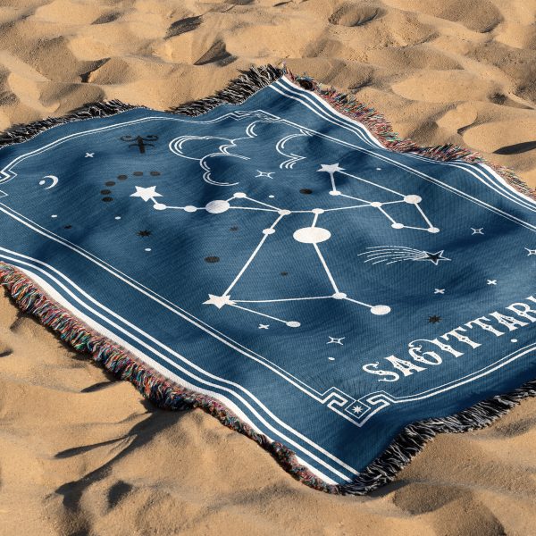 The zodiac woven blanket lies on the sand