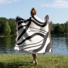 A person standing near a lake on the grass, wrapped in the Scandinavian Abstract Woven Blanket.