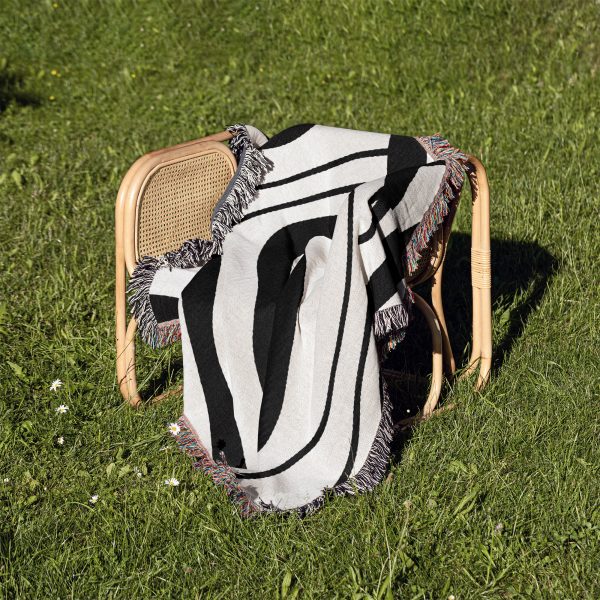 The Scandinavian Abstract Woven Blanket folded neatly on a chair outdoors on a grassy surface.