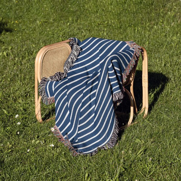 The Scandinavian Blue Striped Woven Blanket folded on a chair outdoors on the grass.