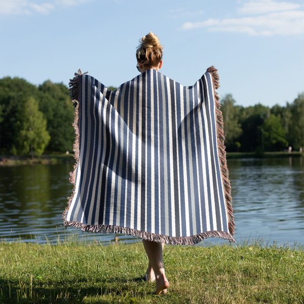 A person wrapped in the Scandinavian Striped Woven Blanket near a lake with grass in the foreground.