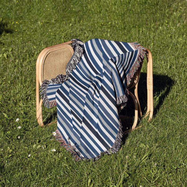 The Scandinavian Striped Woven Blanket neatly folded on a chair outdoors on the grass.