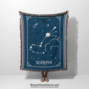 A person holding a Scorpio zodiac woven blanket, featuring deep reds and purples with a scorpion constellation design.