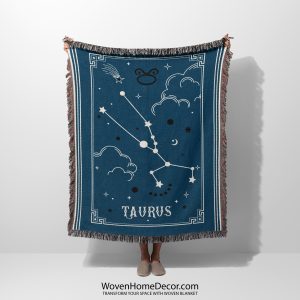 A person holding a Taurus zodiac woven blanket, featuring earthy tones and the Taurus constellation surrounded by soft, celestial patterns.