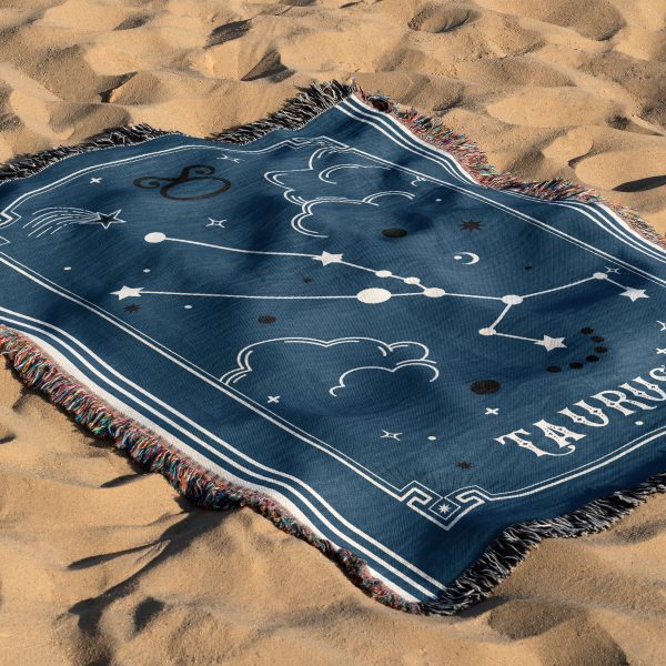 The zodiac woven blanket lies on the sand