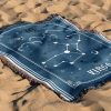 The zodiac woven blanket lies on the sand