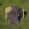 An African-patterned woven blanket draped over a chair outdoors on grassy ground.