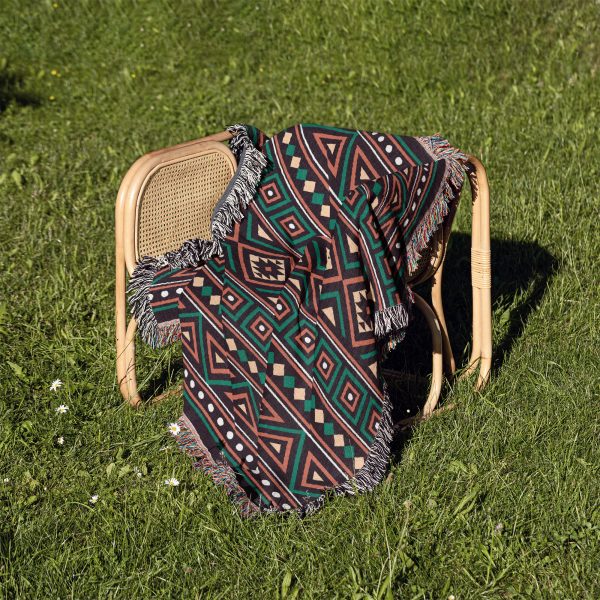 An African-patterned woven blanket draped over a chair outdoors on grassy ground.