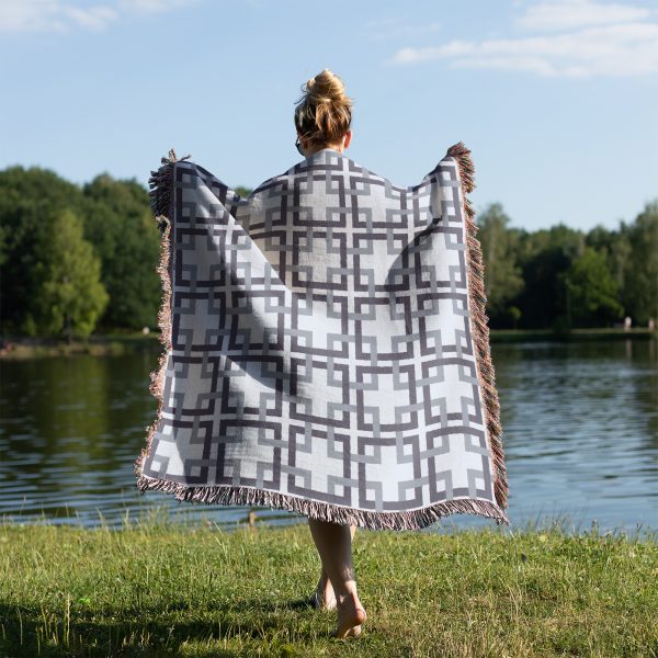 Woman standing with her back to the camera, covering herself with the woven lattice blanket on grass by a lake.