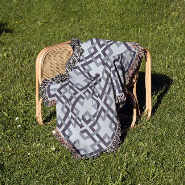 Woven blanket draped over a chair placed on grass, displaying the lattice pattern in calming colors.